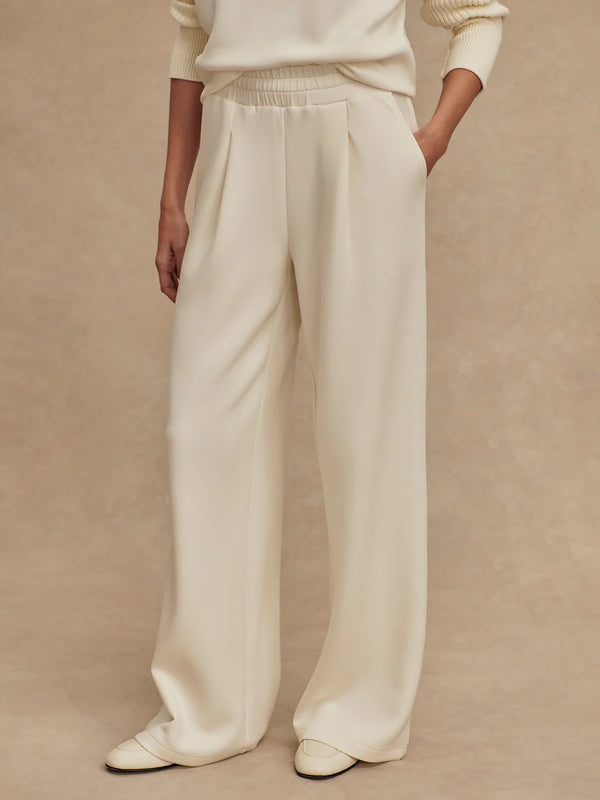 Person wearing a white outfit with wide-leg pants on a beige background