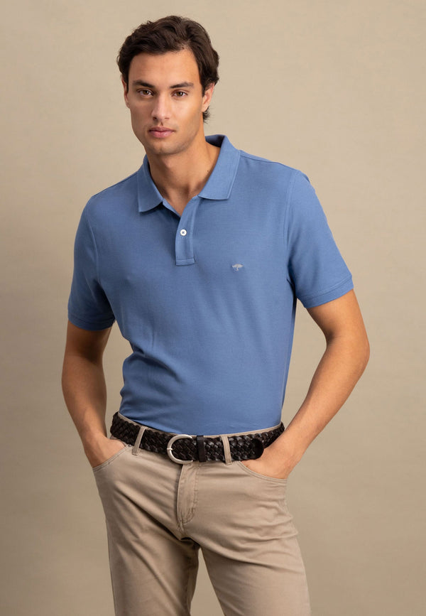 Man wearing a blue polo shirt and beige pants against a neutral background