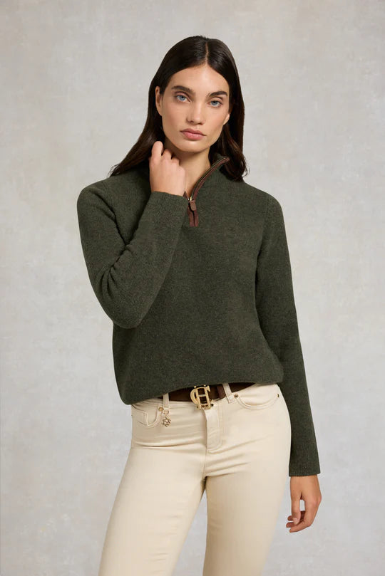 Woman wearing a green sweater and beige pants against a plain background
