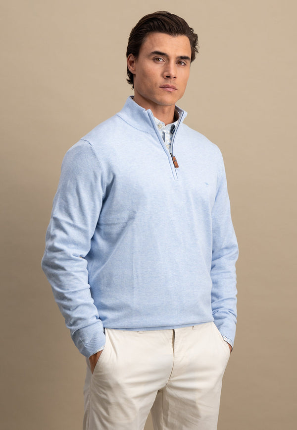 Man wearing a light blue quarter-zip sweater over a white shirt with beige pants on a beige background