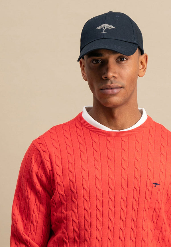 Man wearing a red sweater and navy cap with a logo on a beige background