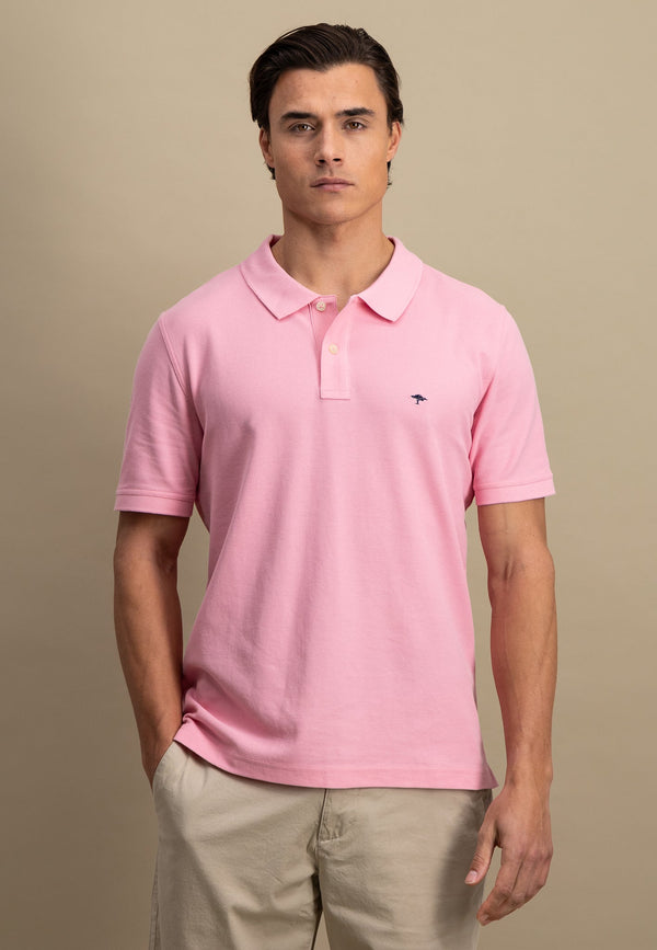 Man wearing a pink polo shirt with a small logo on a beige background