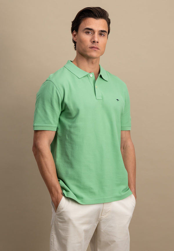 Man wearing a green polo shirt with a small logo on a beige background