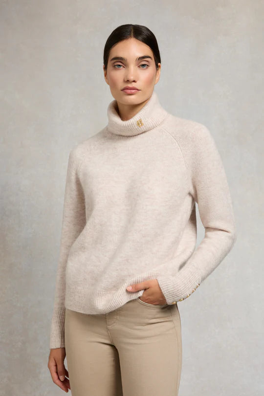 Woman wearing a beige turtleneck sweater and pants against a plain background