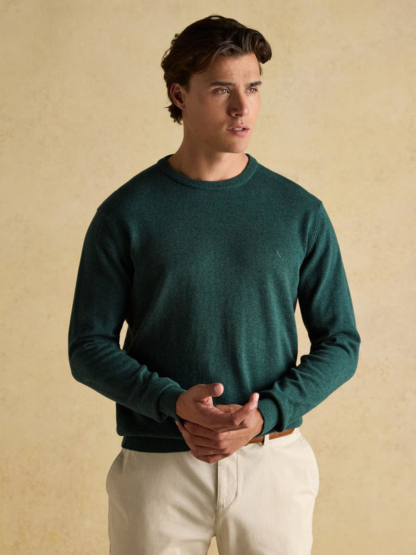Man wearing a green sweater and white pants against a beige background