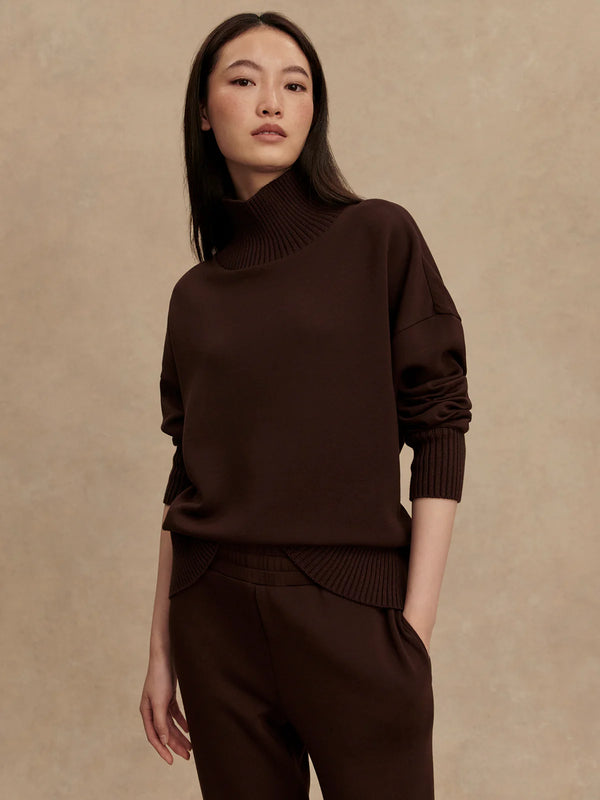 Woman wearing a brown turtleneck sweater and pants against a beige background