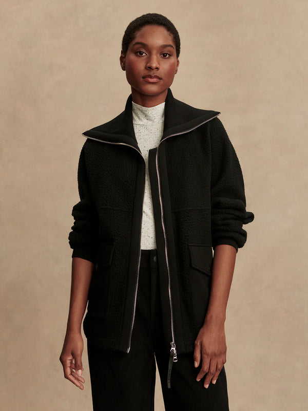 Person wearing a black jacket with a beige background