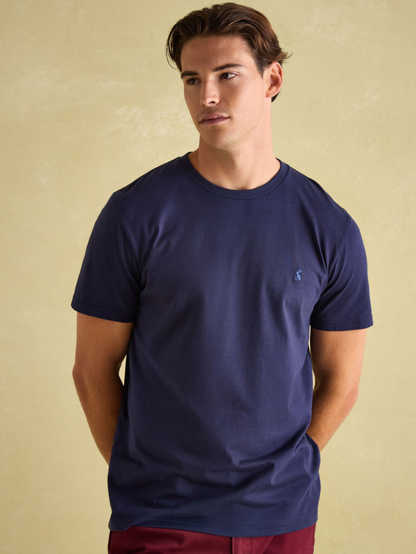 Man wearing a navy blue t-shirt with a small logo on a beige background