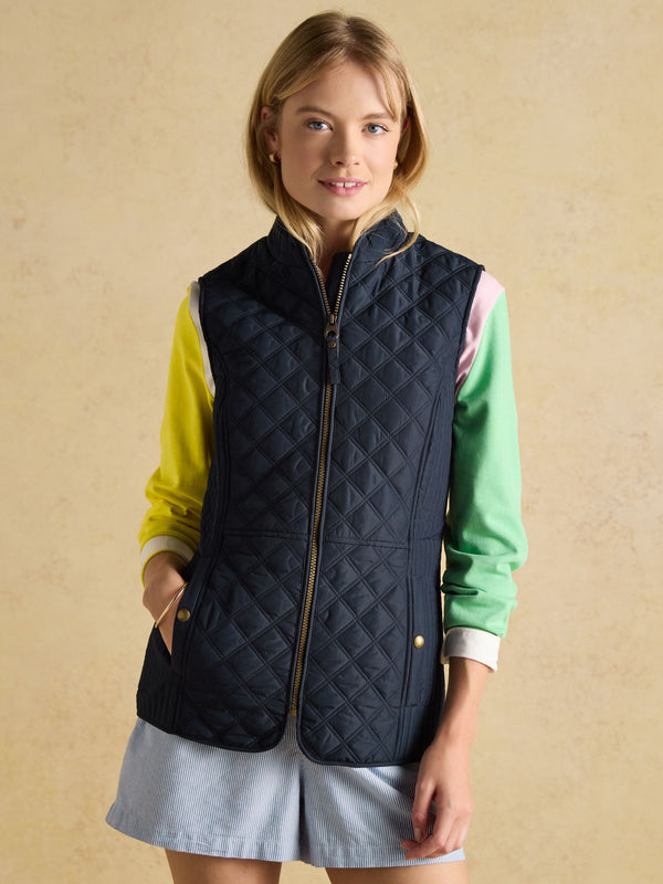 Woman wearing a navy quilted vest over a colorful outfit on a beige background