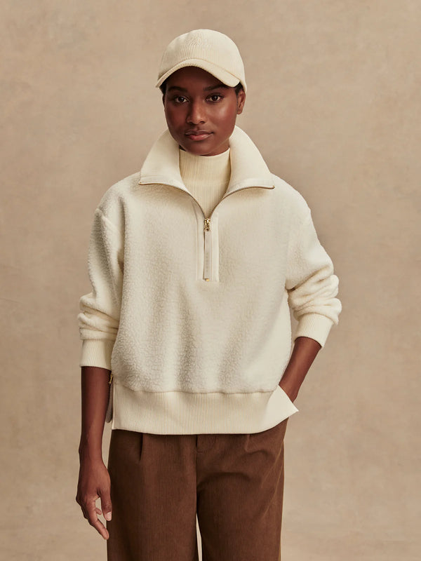 Person wearing a cream-colored sweater and cap against a beige background