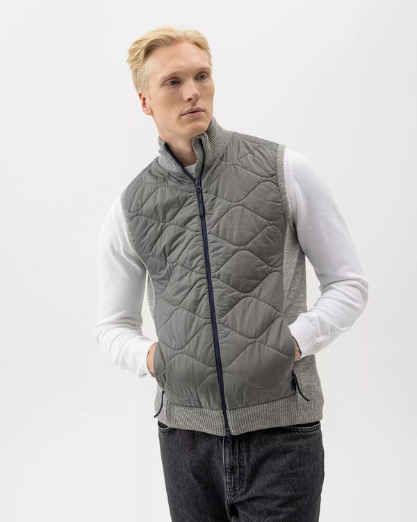 Man wearing a gray quilted vest over a white shirt on a light gray background