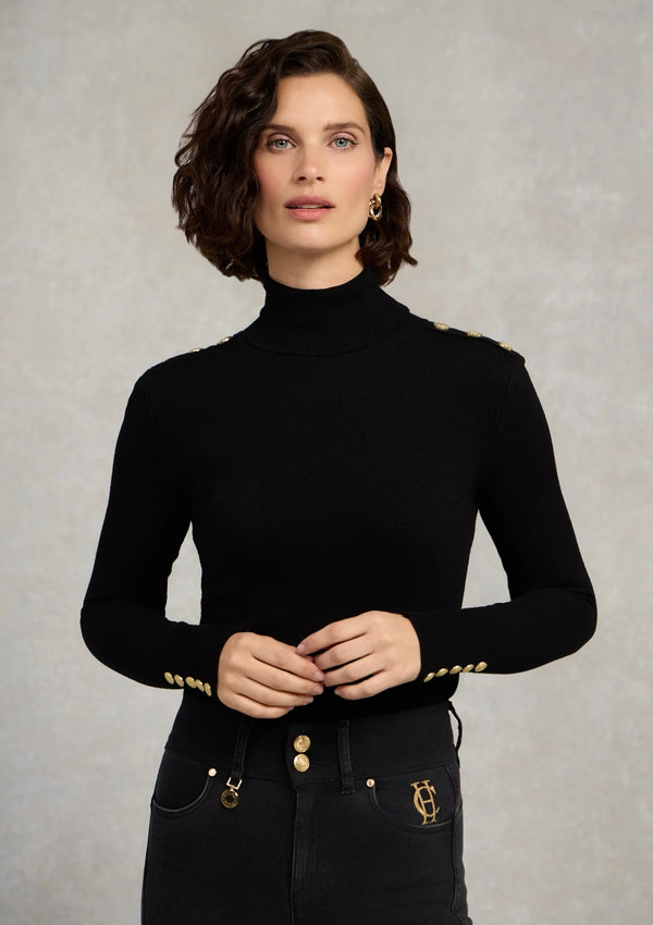 Woman wearing a black turtleneck with gold accents against a neutral background