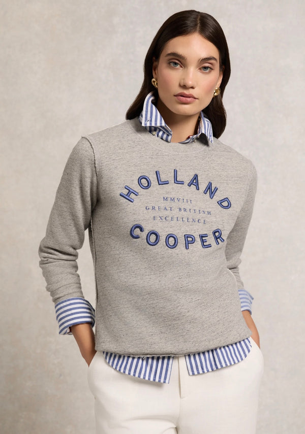 Woman wearing a gray sweater with 'Holland Cooper' branding on a beige background