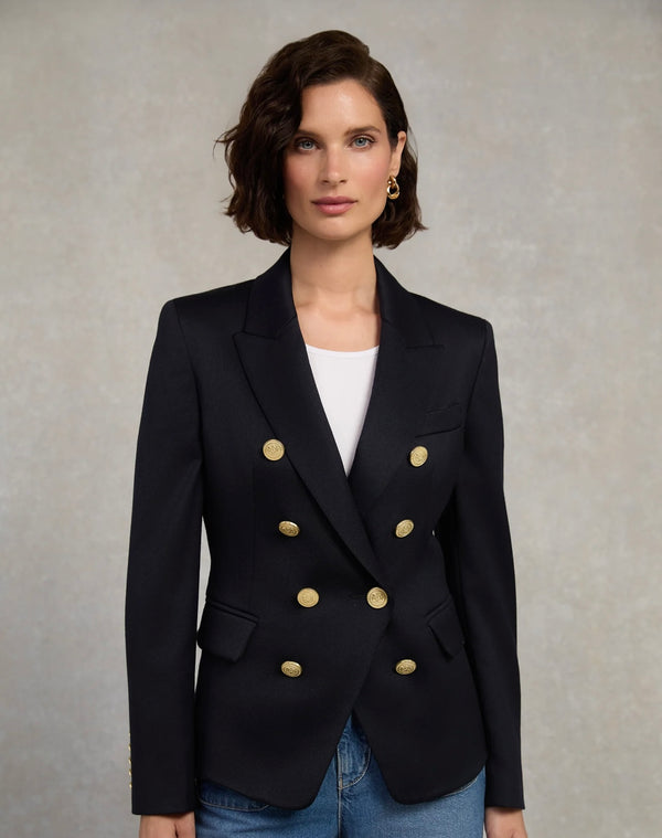 Woman wearing a black blazer with gold buttons on a neutral background