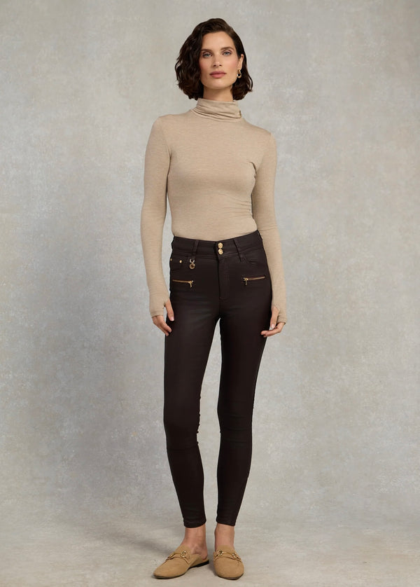 Woman wearing a beige turtleneck and dark jeans against a plain background