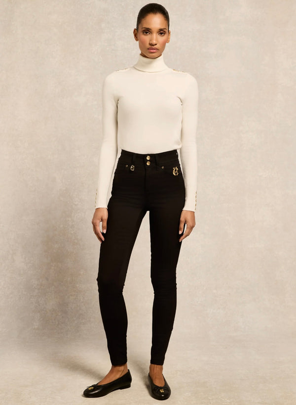 Person wearing a white turtleneck and black high-waisted jeans on a neutral background