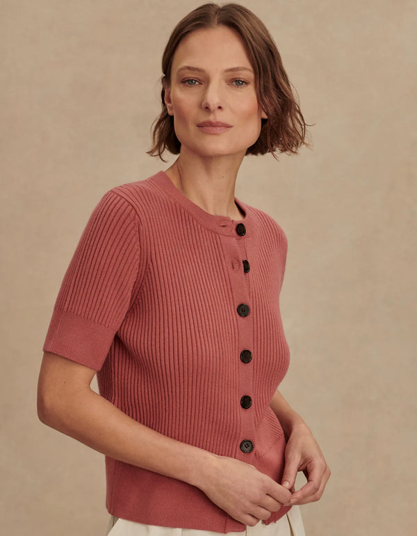 Woman wearing a pink ribbed sweater with black buttons against a beige background
