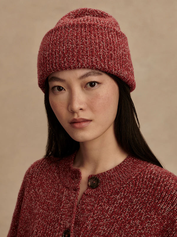 Woman wearing a red knitted hat and sweater against a beige background