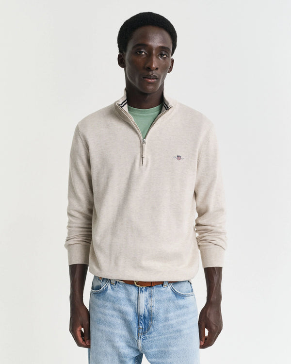 Man wearing a beige sweater and light blue jeans against a white background