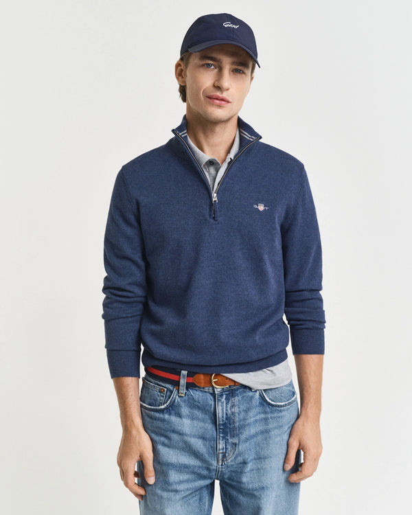 Man wearing a blue sweater, cap, and jeans on a light gray background