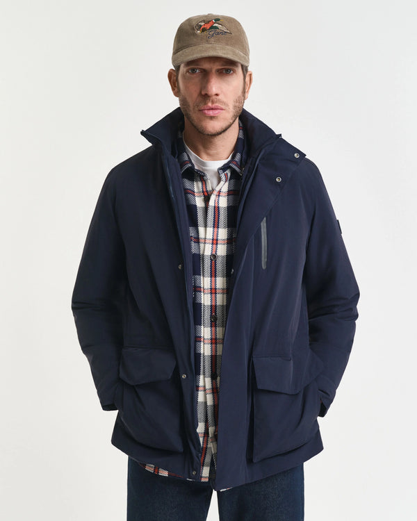 Man wearing a navy jacket over a plaid shirt with a beige cap on a white background