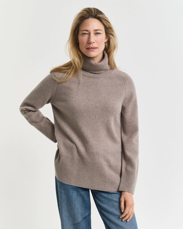 Woman wearing a beige turtleneck sweater and blue jeans on a white background