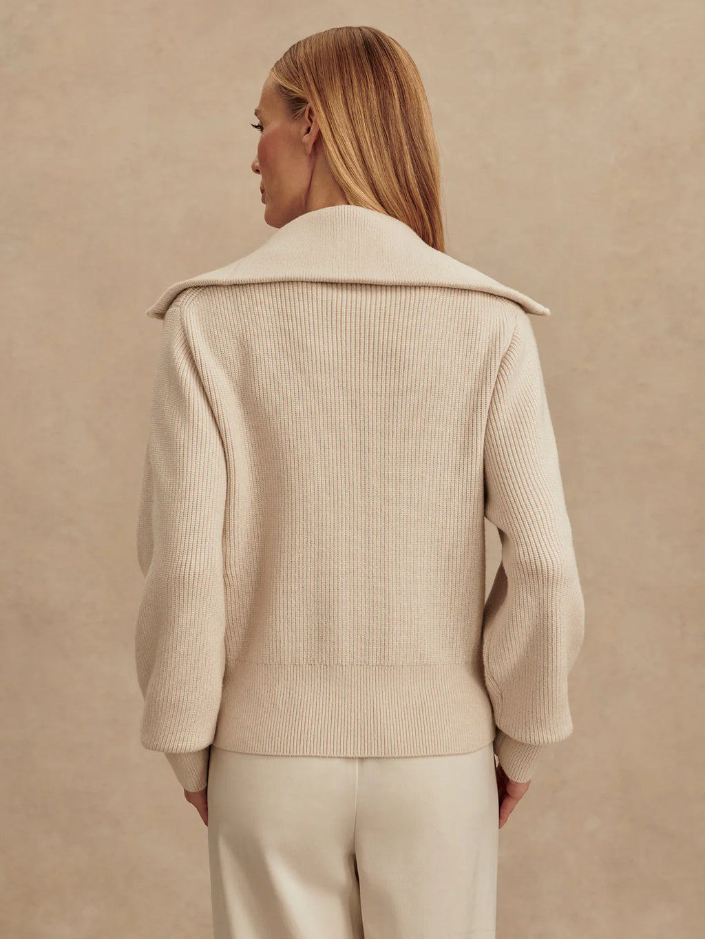 Woman wearing a beige ribbed sweater against a beige background