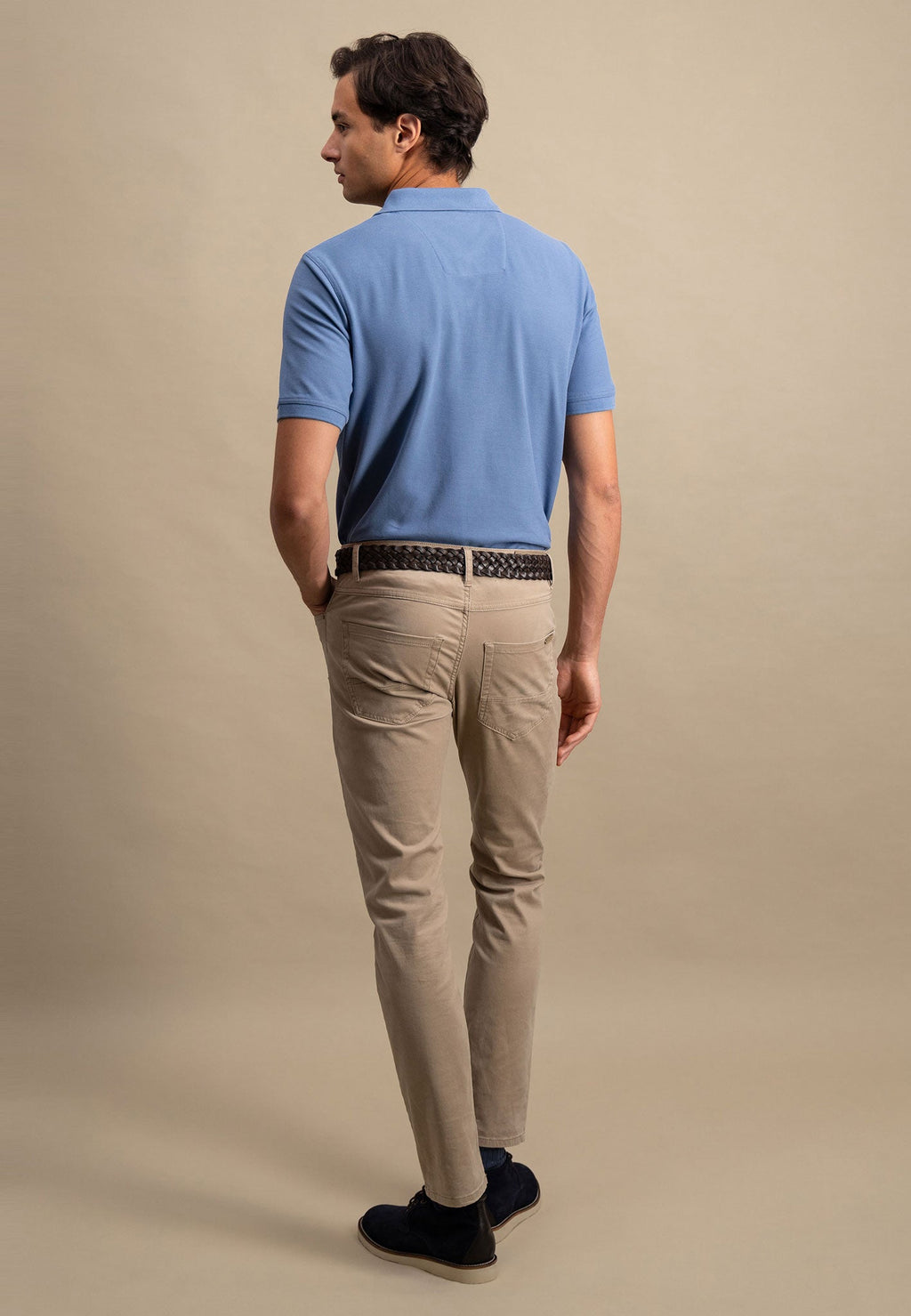 Man wearing a blue polo shirt and beige pants against a beige background