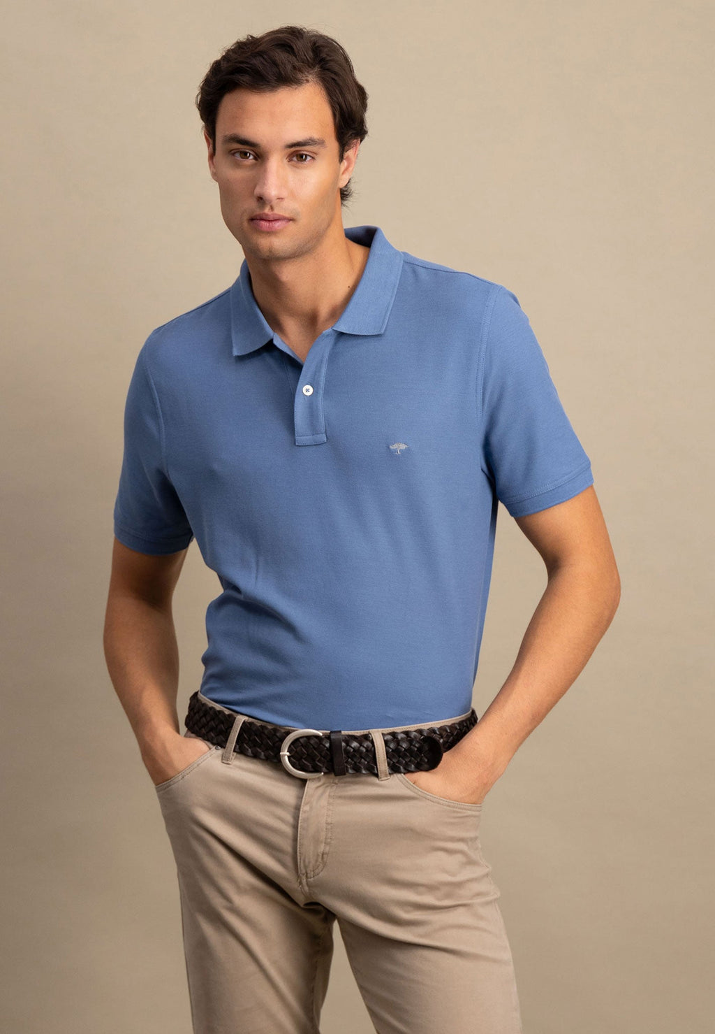 Man wearing a blue polo shirt and beige pants against a neutral background