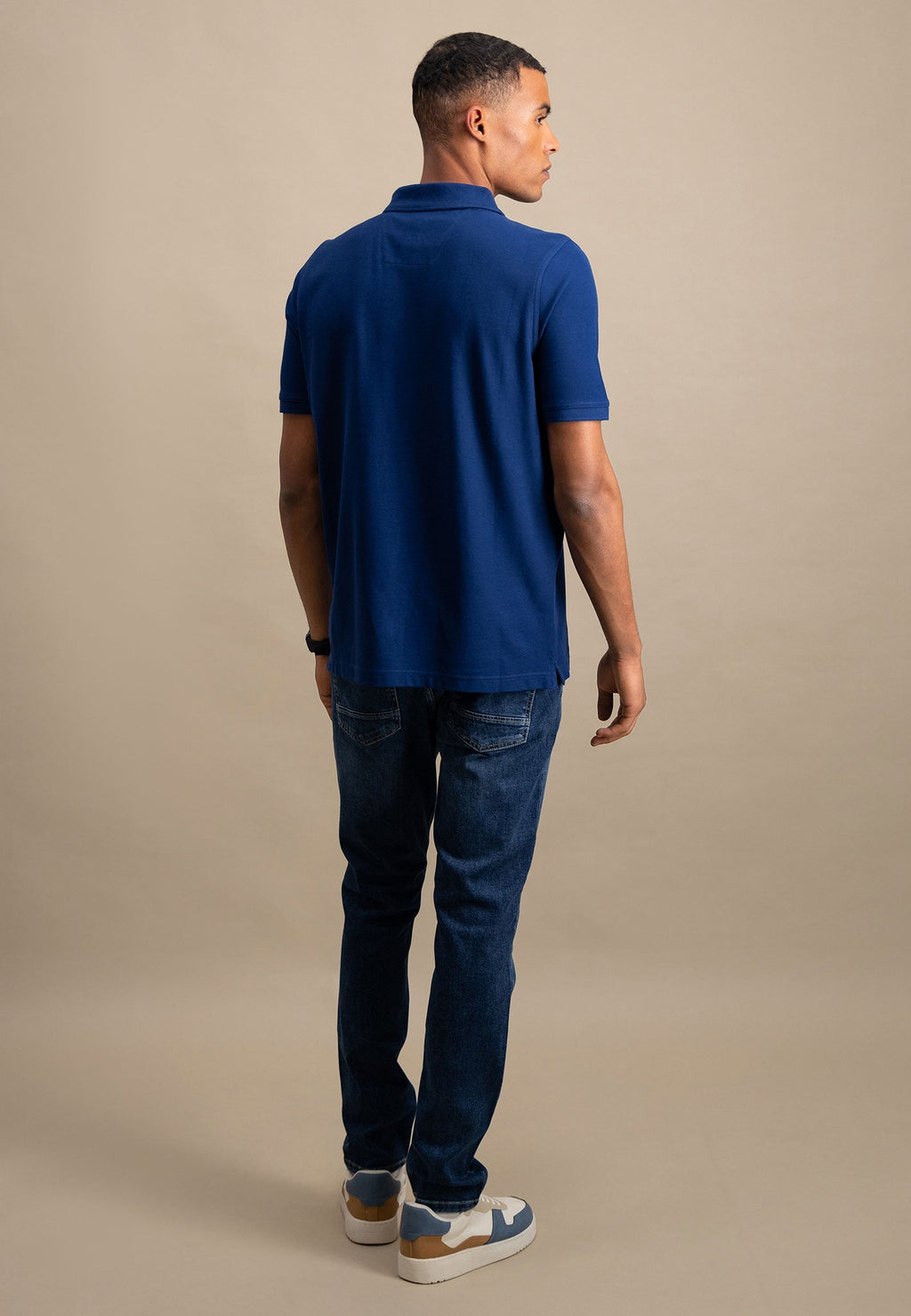 Man wearing a blue polo shirt and jeans on a beige background