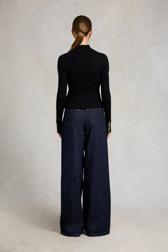 Person wearing a black long-sleeve top and navy wide-leg pants against a plain background