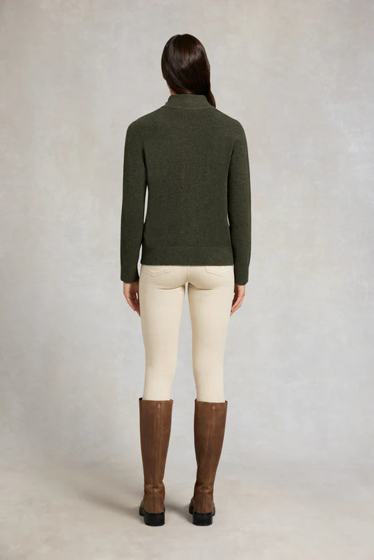 Woman wearing a green sweater, cream pants, and brown boots against a plain background