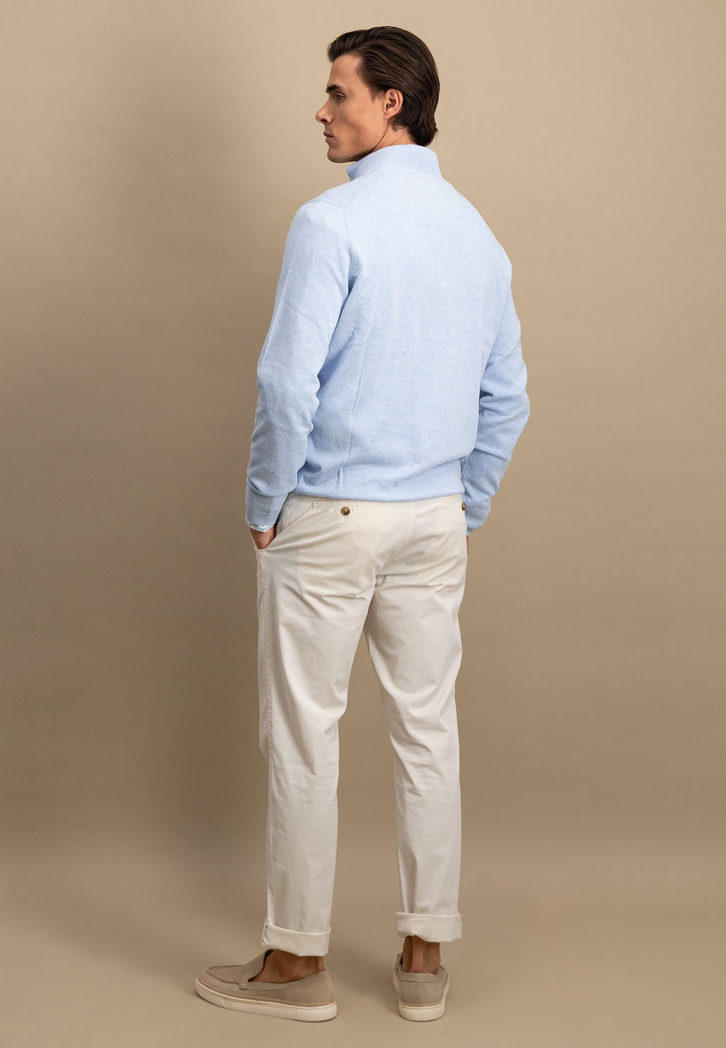 Man wearing a light blue shirt and beige pants against a beige background