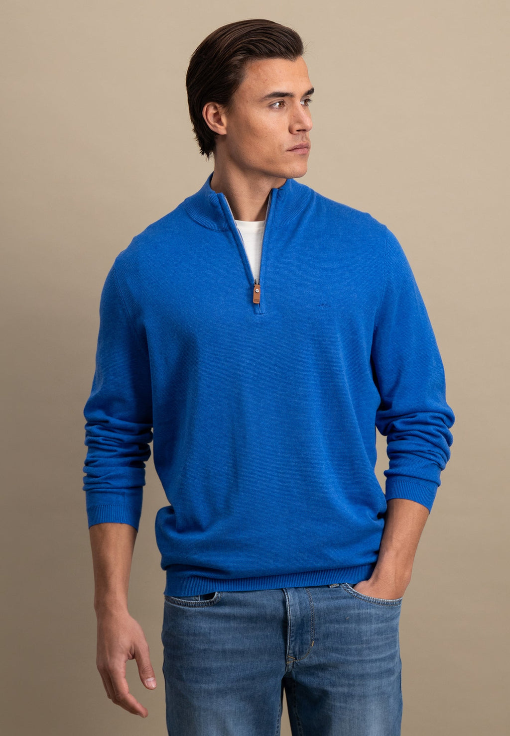 Man wearing a blue sweater and jeans against a beige background