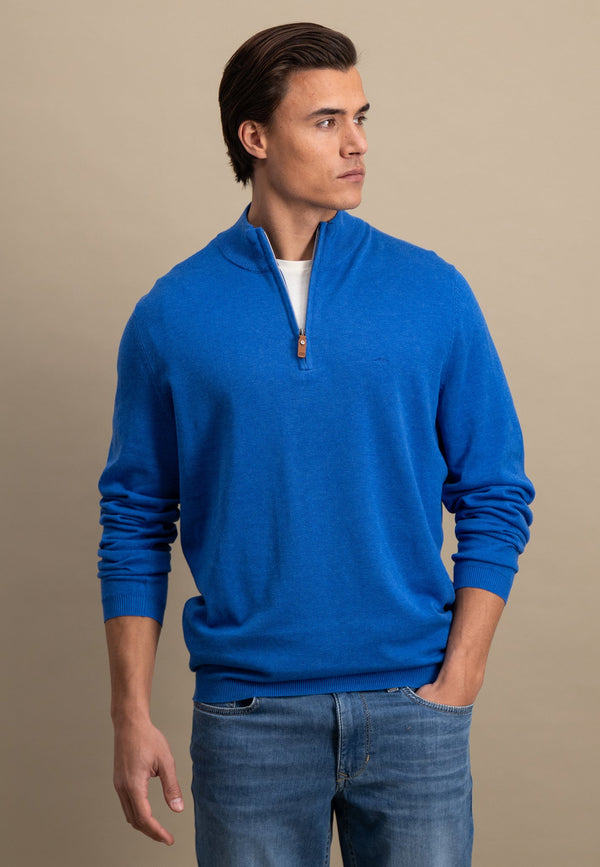 Man wearing a blue sweater and jeans against a beige background