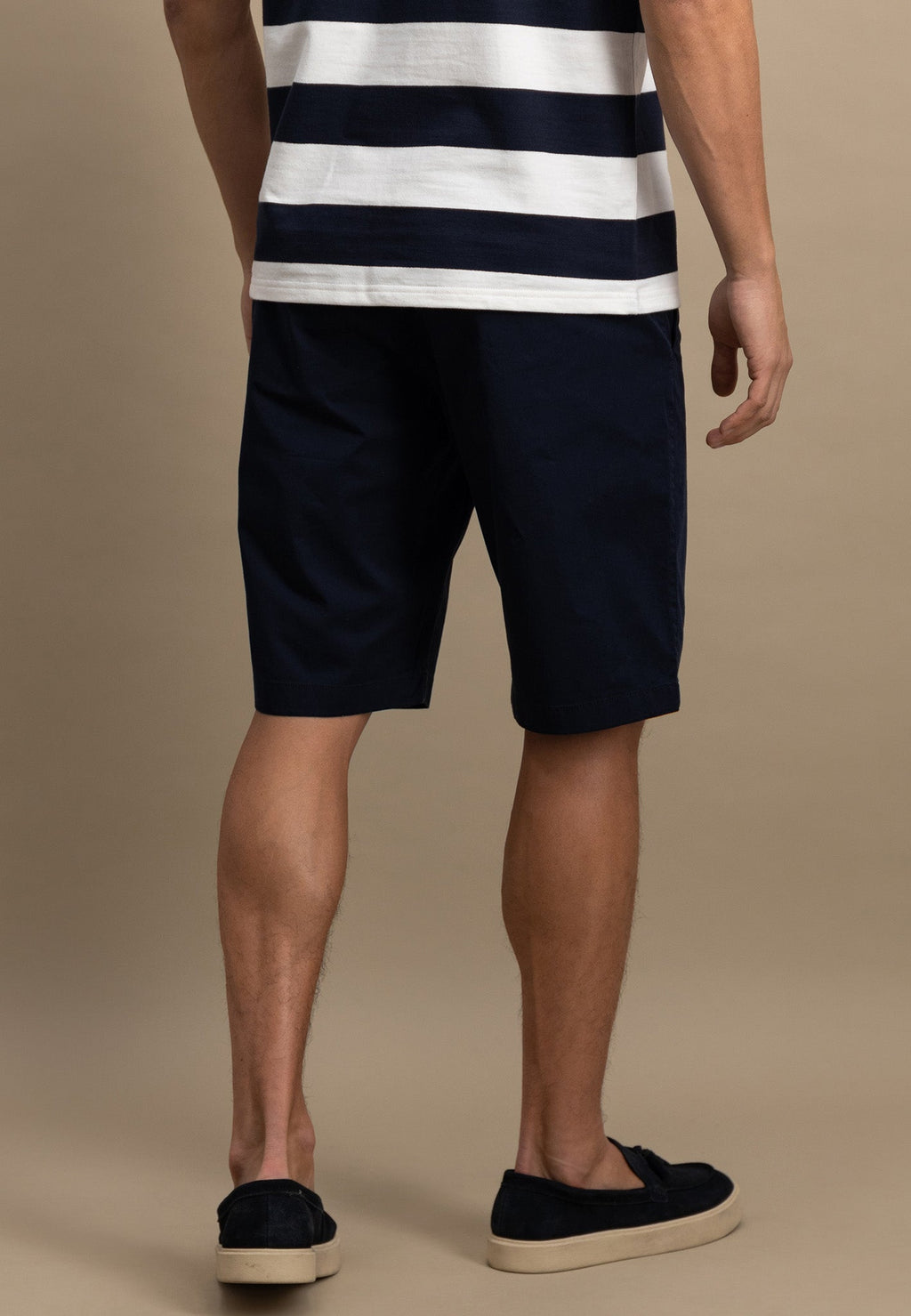 Person wearing navy and white striped shirt with navy shorts on a beige background