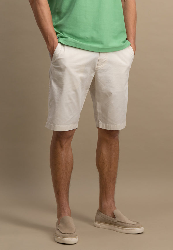 Person wearing a green shirt, white shorts, and beige shoes on a brown background