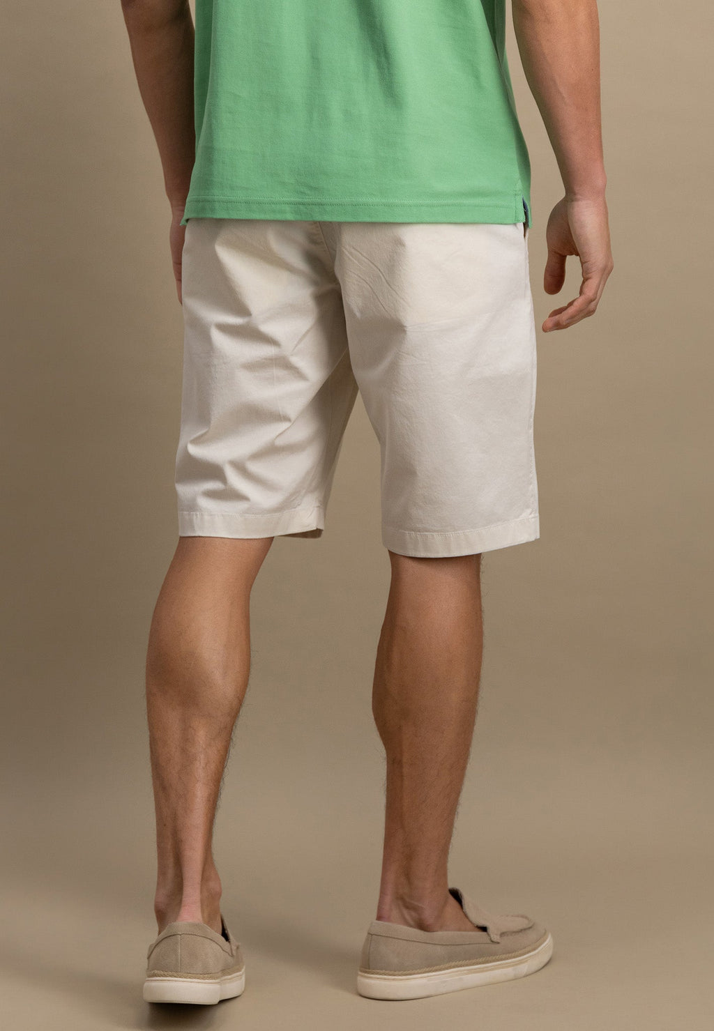 Person wearing a green shirt and beige shorts on a brown background