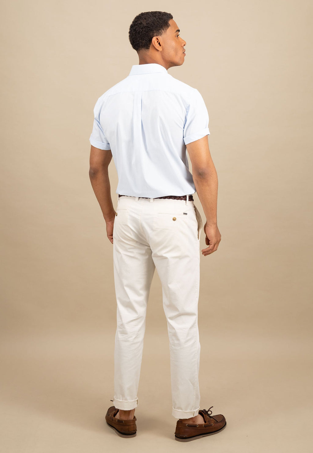 Man wearing a light blue polo shirt and white pants against a beige background