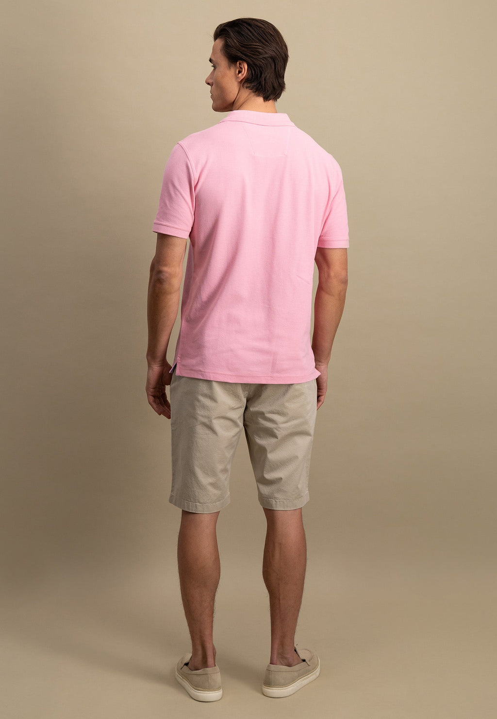 Man wearing a pink polo shirt and beige shorts against a beige background