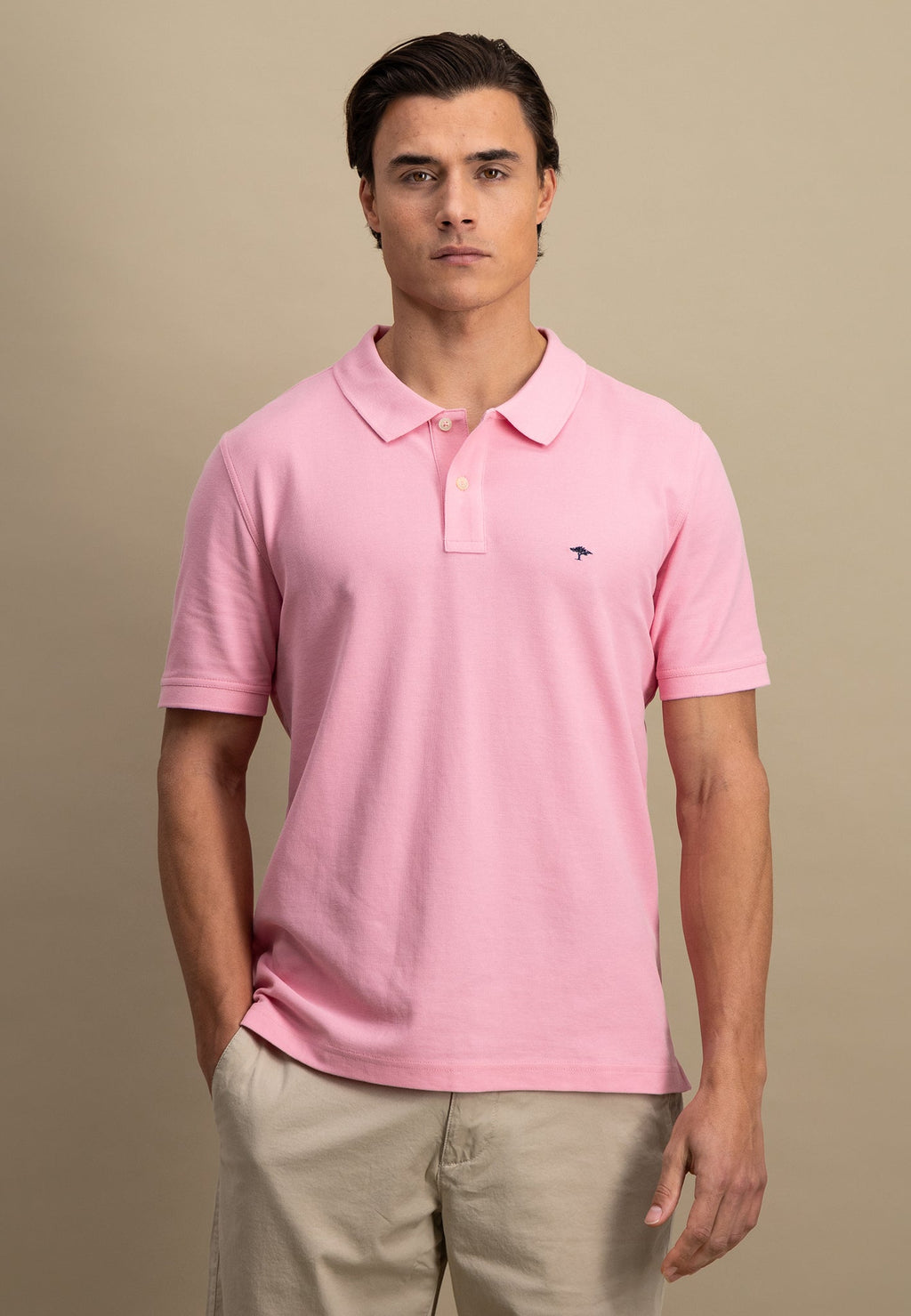 Man wearing a pink polo shirt with a small logo on a beige background