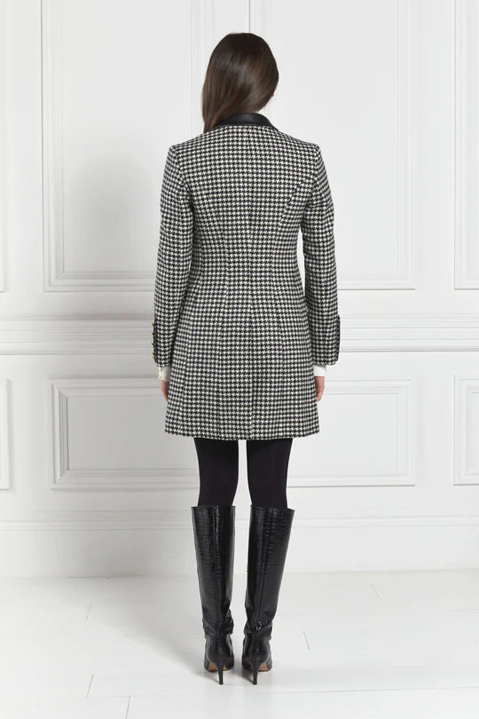 Person wearing a checkered coat and black boots against a white wall