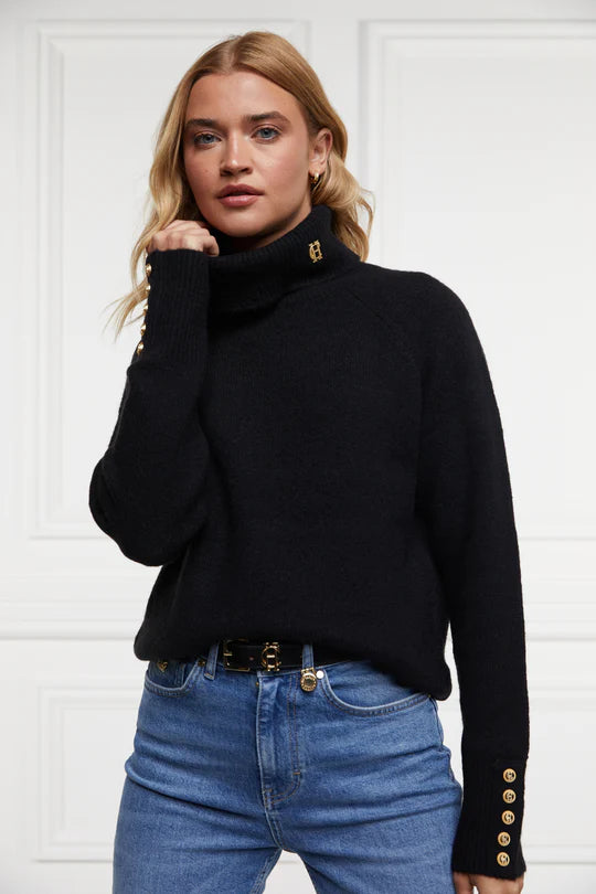 Woman wearing a black turtleneck sweater with gold buttons and blue jeans against a white background