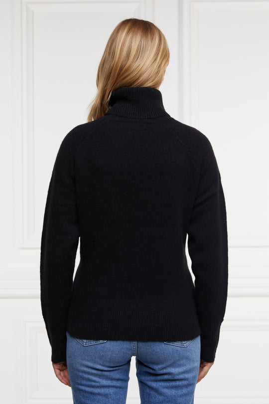 Person wearing a black sweater and blue jeans against a white background
