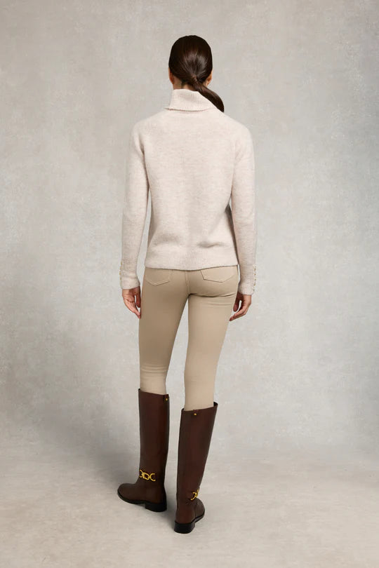 Person wearing a beige sweater, beige riding pants, and brown riding boots on a plain background