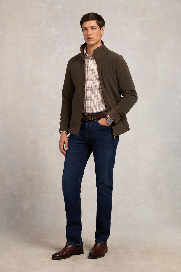 Man wearing a brown jacket, plaid shirt, and blue jeans against a neutral background