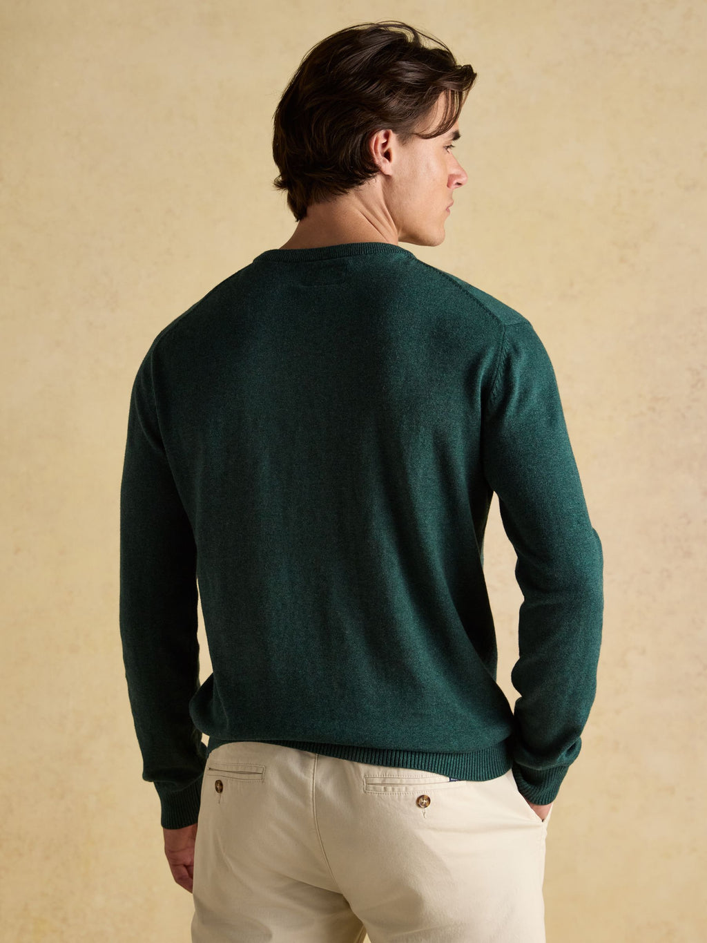 Man wearing a green sweater and beige pants against a beige background