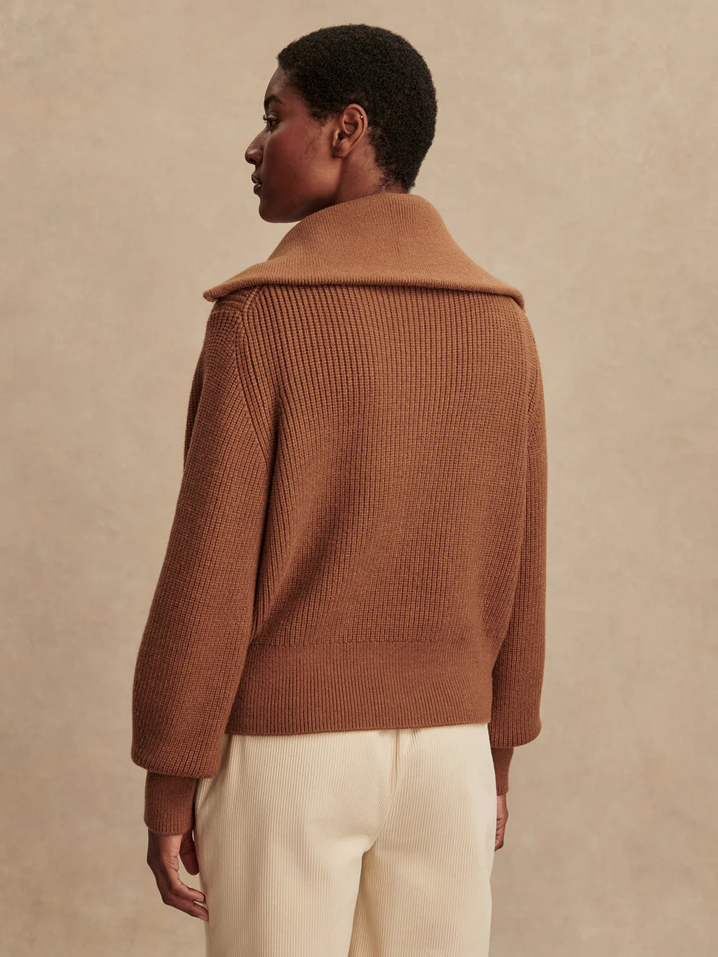 Person wearing a brown knitted cardigan against a beige background