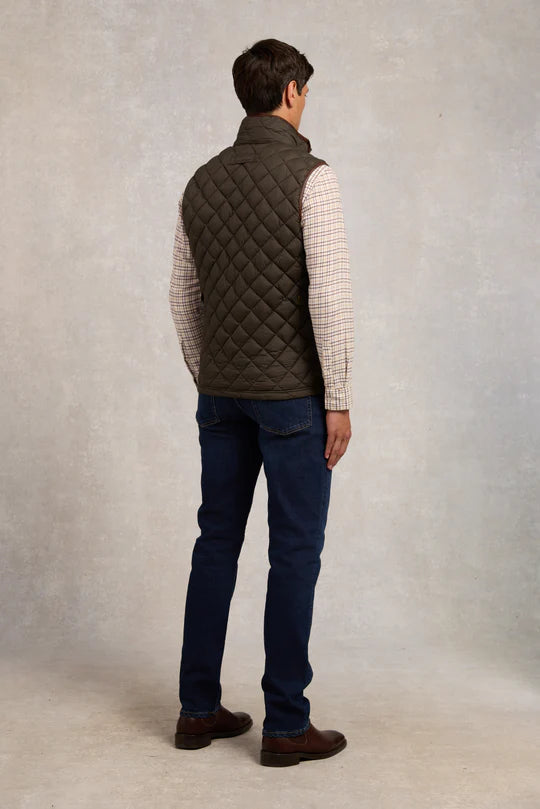 Man wearing a quilted vest, checkered shirt, and jeans against a plain background