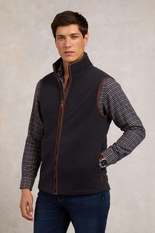 Man wearing a black vest with plaid sleeves on a neutral background